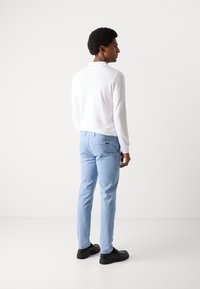 Weißes Langarmhemd kombiniert mit hellblauen Hosen und schwarzen Schuhen. Sichtbare Nähte an den Hosen mit einem Detail an der Gesäßtasche.