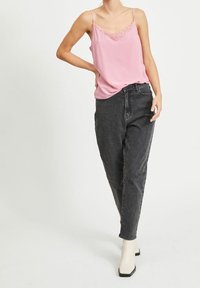 Růžový saténový top s krajkovým lemem, spárovaný s černými džínami s vysokým pasem. Modelka má na sobě bílé kotníkové boty. Neformální oblečení.