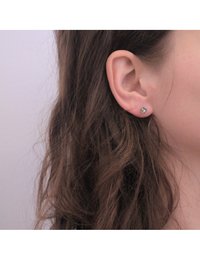 Boucles d'oreilles en argent avec un centre en cristal clair rond, montées sur une base en métal lisse. Portées sur l'oreille d'un mannequin avec de longs cheveux bruns.