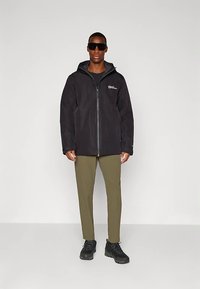 Black jacket with a zip closure and hood, paired with olive green pants and black shoes. Features logo on the chest and sunglasses.