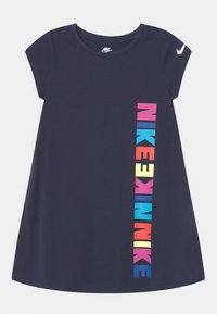 Námořnická modrá krátkosrstá šaty Nike s barevným vertikálním textem "NIKE" na přední straně a bílým logem Nike swoosh na levém rukávu.