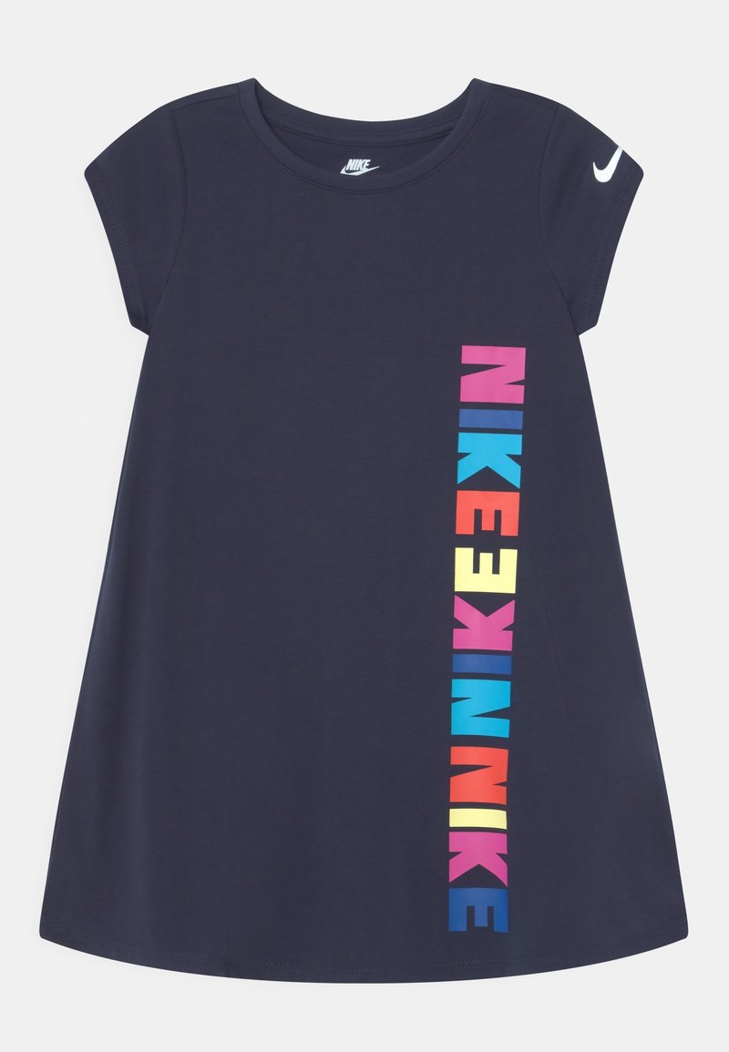 Námořnická modrá krátkosrstá šaty Nike s barevným vertikálním textem "NIKE" na přední straně a bílým logem Nike swoosh na levém rukávu.
