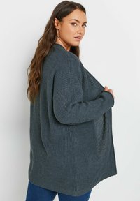 Cardigan lavorato a maglia grigio scuro, dalla vestibilità ampia, in tessuto testurizzato, con maniche lunghe e apertura frontale. Presenta una lieve costina e spacchi laterali.