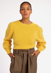 Geel donzig sweater met ronde halslijn en ballonslokken, gecombineerd met bruin hoge taillebroeken met een gestrikte riemdetail.