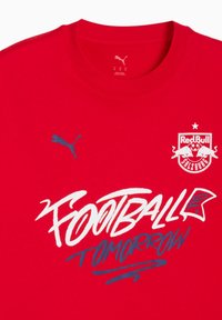 Rød kortærmet t-shirt i bomulds materiale. Har blå Puma-logo, hvid tekst "FOOTBALL TOMORROW" og Red Bull Salzburg-emblem.