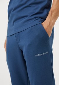 Σκούρο μπλε φόρμες joggers από βαμβακερό μείγμα με πλάγια τσέπες και λευκό λογότυπο "BJÖRN BORG" στο κάτω αριστερό πόδι. Λείο ύφασμα, άνετη εφαρμογή.