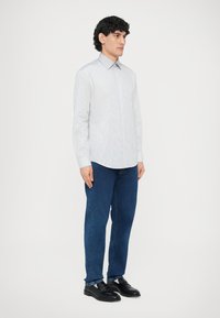 Biała i niebieska koszula w paski z długim rękawem i kołnierzykiem, w połączeniu z niebieskimi dżinsami i czarnymi mokasynami. Gładka tkanina i dopasowany krój.