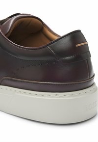 Sneaker in pelle marrone scuro con superficie testurizzata, suola in gomma bianca e un sottile accento beige sul tallone. Presenta cuciture decorative.