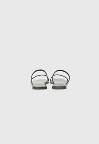 Sorte flate sandaler med to tynne, kryssede stropper, et minimalistisk design, og en glatt, flat såle. Enkel og lett konstruksjon.