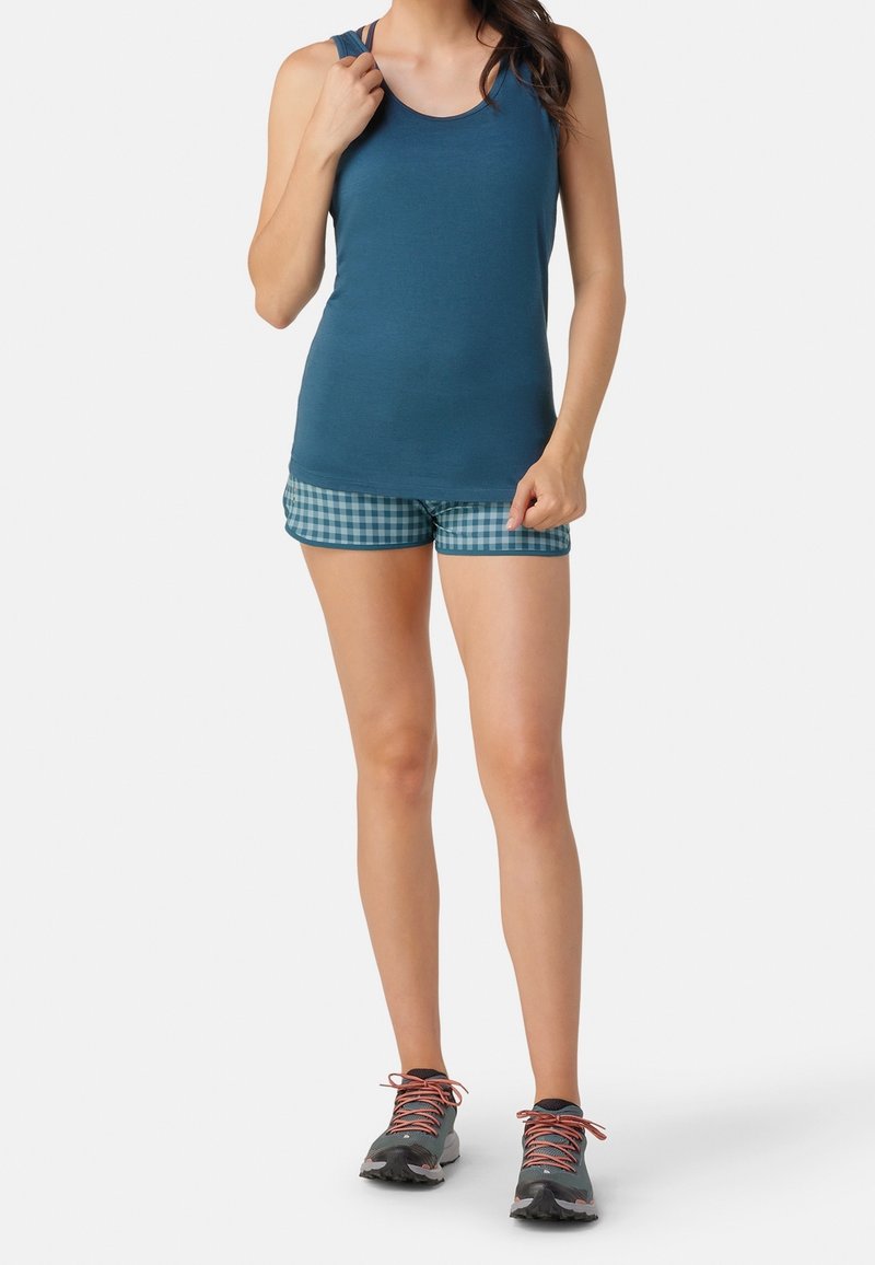 Canottiera blu abbinata a pantaloni corti a quadri blu e verdi. Il modello indossa sneakers grigie con lacci arancioni. Tessuto morbido, stile atletico casual.