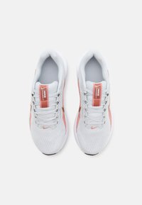 Bílé sportovní boty s prodyšným síťovaným svrškem, růžovými akcenty, plochými tkaničkami a malým oranžovým logem swoosh na špičce a jazyku.