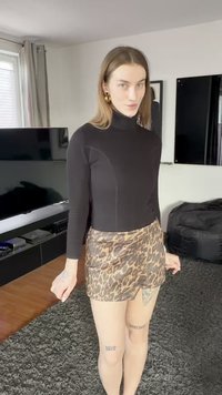 Zwarte coltrui met lange mouwen gecombineerd met een korte rok met luipaardprint. Kenmerkt zich door een aansluitend ontwerp en een gladde textuur. Accessoires omvatten grote oorbellen.