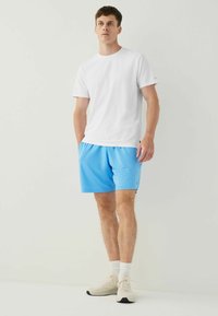 White short-sleeve t-shirt paired with light blue athletic shorts, textured fabric, and pale sneakers with a black sole.