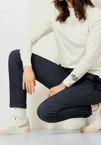Marineblauwe broek met een slim fit, gecombineerd met een crèmekleurig sweatshirt. Witte sneakers accentueren de outfit.