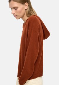 Rdzawoczerwony, dzianinowy hoodie o luźnym kroju, z kapturem na sznurki, szerokimi rękawami i miękką teksturą.