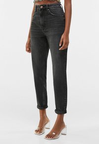 Černé džíny s vysokým pasem, tapered střihem, ohrnutými manžetami a kontrastním šitím. V kombinaci s průhlednými sandály na podpatku.