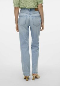 Ανοιχτό μπλε τζιν παντελόνι με ίσια κοπή, που διαθέτει πίσω τσέπες και δερμάτινη επιγραφή στη μέση; φορεμένο με κρέμ ψηλοτάκουνα παπούτσια.