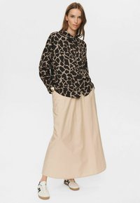 Majica s leopard printom u crnoj i bež boji, opuštenog kroja; krem maxi suknja; bijele tenisice s crnim detaljima. Glatka tekstura tkanine.