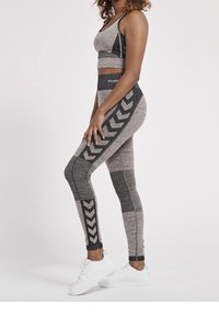 Top corto sportivo grigio e leggins con un motivo testurizzato e design a chevron, abbinati a scarpe da ginnastica bianche.