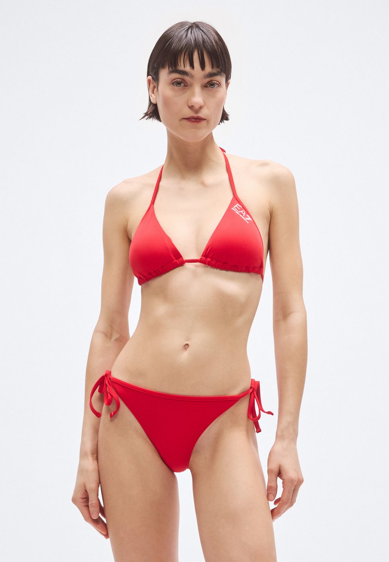 Bikini rosso con top triangolare e slip con laccetti ai fianchi, realizzato in tessuto liscio, con un marchio discreto sulla fascia del top.