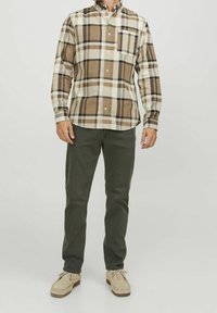 Camisa de cuadros marrón y beige con cuello abotonado, mangas largas, bolsillo en el pecho, combinada con pantalones verde olivo y zapatos de un beige claro.