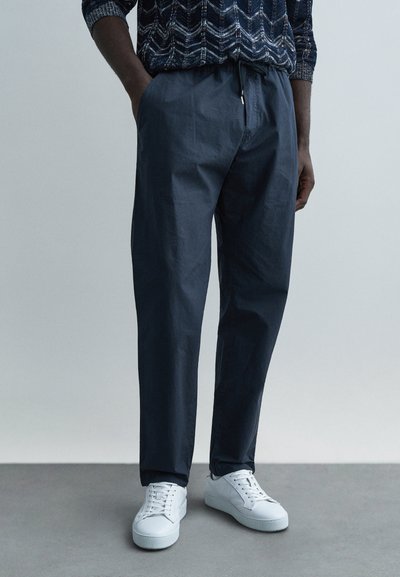 Navy lightweight pants with a relaxed fit, elastic waistband, and side pockets, paired with white sneakers on a gray surface.