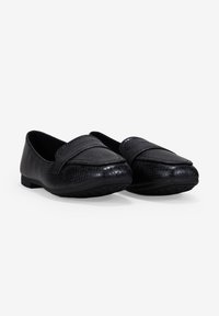 Zapatos de mocasín negros con un patrón texturizado que asemeja reptiles. Material suave, suela plana y una correa prominente en la parte delantera. Diseño de punta redonda.