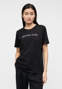 T-shirt preta de algodão com decote redondo e mangas curtas, com "MICHAEL KORS" em strass prateados no peito.