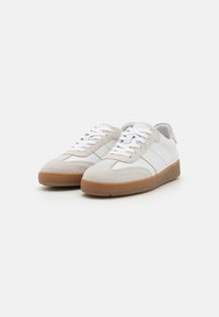 Sneaker bianchi e grigi con tomaia in suede e pelle, punta rotonda, lacci bianchi e suola in gomma marrone chiaro.