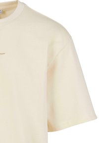 Short-sleeve t-shirt in cream organic cotton, featuring a rounded neckline and subtle stitching detail across the chest. Soft, smooth texture.