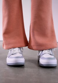 Staubige rosa weite Sweatpants mit genähten Säumen, kombiniert mit weißen und hellgrauen Sportschuhen, die über Lochdetails und Schnürsenkel verfügen.