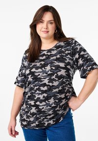 T-shirt à motif camouflage gris en tissu doux, avec des manches courtes et un col rond, porté avec un jean bleu.