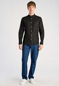 Czarna koszula z długim rękawem z kołnierzem typu stójka i białymi guzikami, zestawiona z niebieskimi dżinsami i białymi trampkami. Prosty fason, gładka faktura.