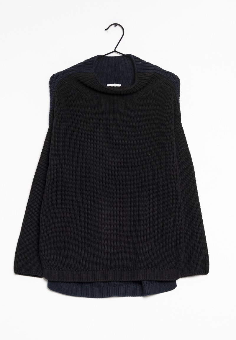 Schwarzer Strickpullover mit gerippter Textur und weitem Kragen, der an einem schwarzen Haken hängt und einen dunkelblauen Pullover darunter überlagert.