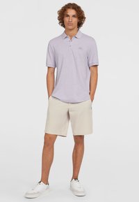 Polo shirt violet clair avec un col, des manches courtes et un logo brodé, associé à un short beige et des baskets blanches.