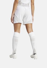 Witte sportshorts met mesh accenten, gecombineerd met witte knielange sokken met een geometrisch patroon en zwarte voetbalschoenen.