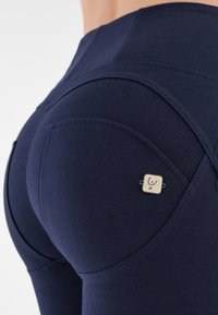 Leggings blu navy con un design aderente, realizzati in un tessuto testurizzato. Presentano un piccolo accento metallico quadrato nell'area della tasca posteriore.