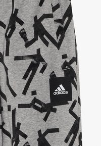 Szare spodnie sportowe z czarnym abstrakcyjnym wzorem, wykonane z miękkiego materiału, z logo Adidas na czarnej łatce.
