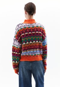 Kolorowy sweter wykonany na drutach z wysokim pomarańczowym kołnierzem i różnorodnymi skomplikowanymi wzorami w kolorach purpurowym, zielonym, niebieskim i czerwonym. Luźny krój.