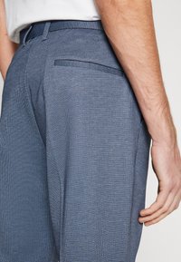 Blå texturerade byxor med smal passform, slät fram och en enkel bakficka med ett subtilt rutmönster.