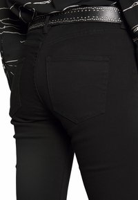 Svarta jeans i denim med en tight passform, med en rundad bakfickedesign och ett glänsande svart bälte med silvernitar.