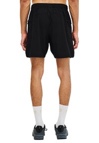 Schwarze Shorts mit elastischem Bund und seitlichen Taschen. Getragen mit grauen Schuhen und weißen Socken, die Text zeigen.
