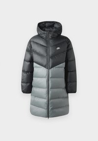 Dug i dužem jaknu s punjenjem koja ima dizajn u crnoj i sivoj boji u blokovima, kapuljaču, zip zatvaranje sprijeda i Nike logo na lijevoj polovici prsnog koša. Glatka tekstura.