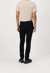 Zwarte slim fit jeans met een gladde textuur, twee achterzakken, gecombineerd met een beige t-shirt met korte mouwen, gedragen met zwarte sportschoenen.