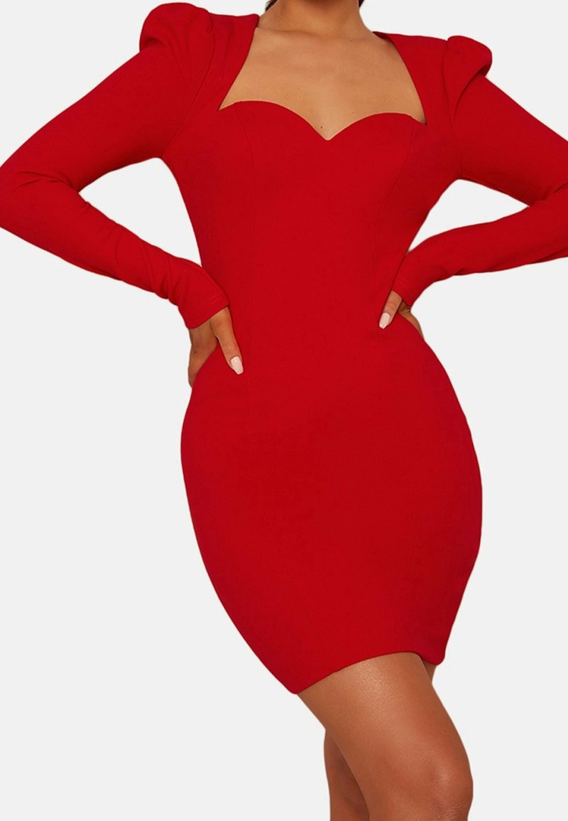 Mini-robe rouge moulante avec manches longues bouffantes et décolleté en cœur portée par une personne les mains sur les hanches.