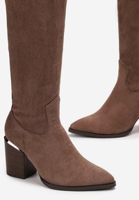 Bottines en daim marron de hauteur genou avec des bouts pointus, une surface texturée et des talons blocs présentant des accents boisés.
