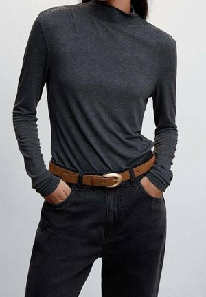 Haut noir à manches longues avec un col montant, assorti à un jean foncé et une ceinture marron avec une boucle argentée.