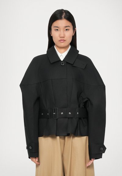 Veste noire cropped avec un large col, des manches surdimensionnées et une taille ceinturée. Inclut une fermeture à boutons et des détails de couture visibles.