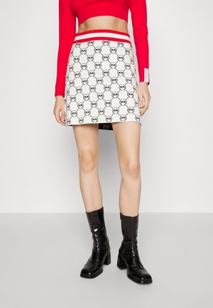 Kvinde iført en hvid mininederdel med sorte cirkelmønstre, rød talje, rød kortærmet langærmet top og sorte støvler med hæl til midt på læggen.