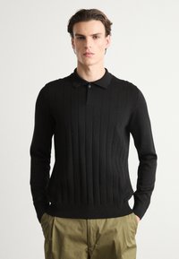 Tricou polo cu mânecă lungă, tricotat în negru, cu textură verticală dreaptă și guler clasic, asortat cu pantaloni kaki.